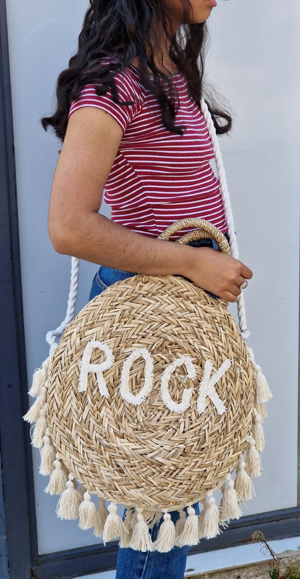 Sac en osier rond avec inscription "rock" au milieu du sac. le contour du sac est rempli de pompons.